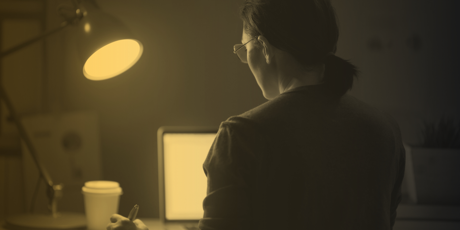 Woman working at her desk late at night with a single lamp and coffee