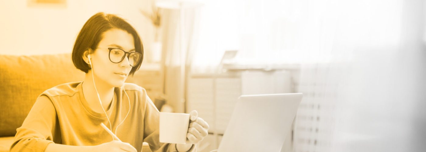 woman holding a coffee mug and looking at a laptop while writing a video transcription